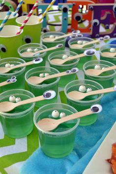 green cups with googly eyes and wooden spoons in them on a tablecloth