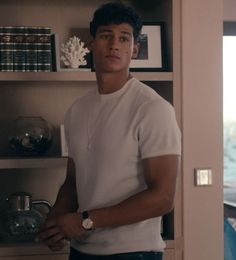 a young man standing in front of a book shelf with books on top of it