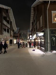 people are walking down the street in front of some buildings at night time with snow on the ground