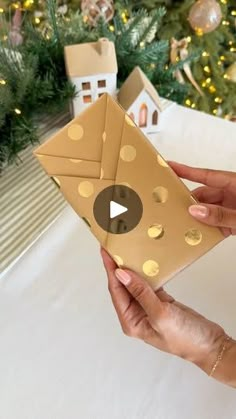 a person holding an origami envelope in front of a christmas tree with gold polka dots