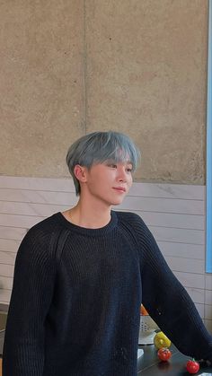 a young man with grey hair standing in front of a counter topped with fruits and vegetables