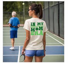 "Embrace your pickleball passion with this Retro Pickleball Mom T-Shirt! Featuring a vintage design, this Pickleball Era Tee is perfect for moms who love hitting the court and showing off their pickleball pride. Made from premium, soft cotton, this shirt offers ultimate comfort whether you're playing a match or cheering from the sidelines. It's a fantastic gift for pickleball moms, sports enthusiasts, or anyone who loves the game. Available in various sizes and colors, this proud Pickleball Mom White Moisture-wicking Tennis T-shirt, White Moisture-wicking T-shirt For Tennis, White Tennis Top With Team Name, Sporty Green T-shirt For Pickleball, Green Sporty T-shirt For Pickleball, Retro Pickleball, Mom Apparel, Pickleball Gifts, Pickleball Gift