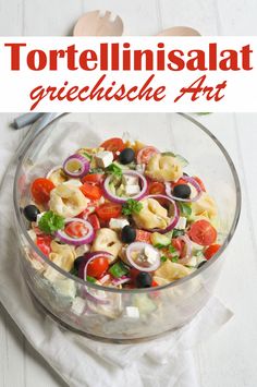 a glass bowl filled with pasta salad on top of a white table