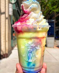 a hand holding up a cup with ice cream and toppings on it in front of a building