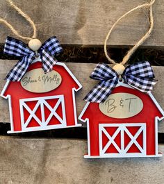 two red barn shaped ornaments with blue and white plaid bows hang from twine on wood planks