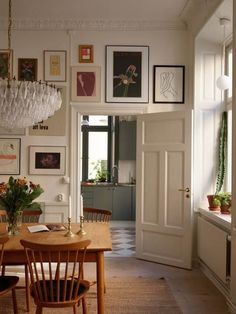 a dining room table with chairs and pictures on the wall above it, in front of a doorway