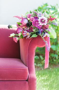 a pink chair with flowers on it sitting in the grass next to a red couch