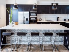 a kitchen with black cabinets and white counter tops, along with bar stools that match the hardwood flooring