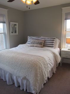 a bedroom with a bed, two windows and a ceiling fan in the middle of it