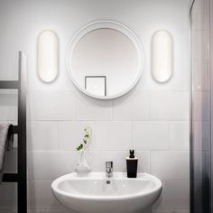 a white sink sitting under a round mirror next to a bathroom counter with a vase on it