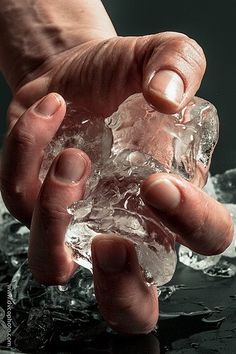 a person holding an ice cube in their hand on top of some water and ice