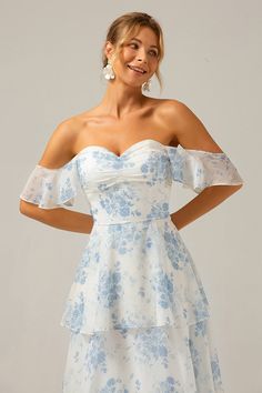 a woman wearing a white and blue floral print dress with off the shoulder ruffle sleeves