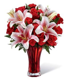 a vase filled with red roses and lilies on top of a white countertop