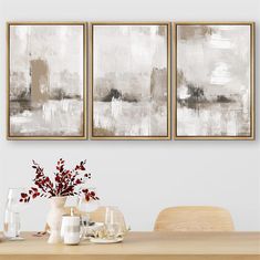 three paintings hang on the wall above a dining room table with white dishes and vases