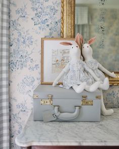 two stuffed animals sitting on top of a suitcase in front of a mirror and wallpaper