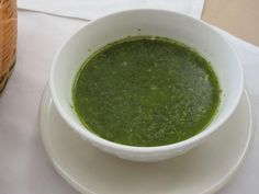 a white bowl filled with green liquid on top of a plate