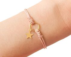 a woman's arm with a gold star charm and pink rope bracelet on it