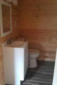 a white toilet sitting next to a sink in a bathroom under wood paneled walls