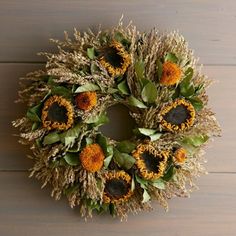 a wreath with sunflowers and green leaves on a wooden surface in front of a wall