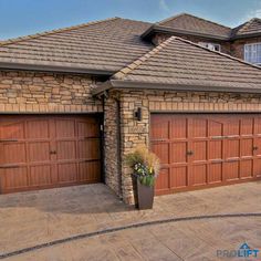 two brown garage doors in front of a brick house with potted plants on the driveway