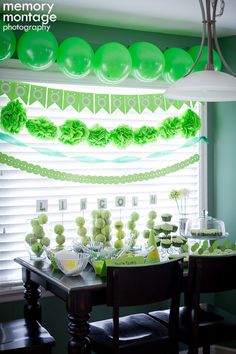 a table set up for a party with balloons and green decorations on the wall behind it