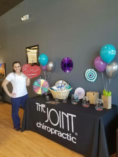 a woman standing in front of a table with balloons and other items on it at the jointt chiropractic