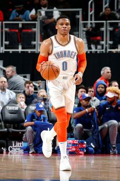 a basketball player with an orange and white uniform is running on the court while fans watch