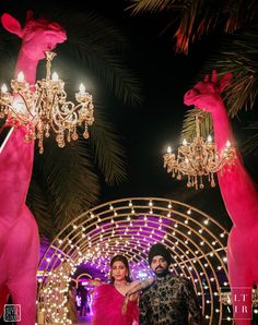 a man and woman standing in front of pink giraffes with chandeliers