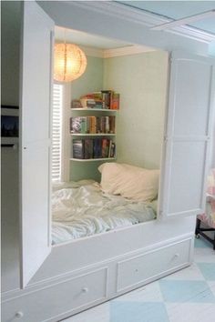 a white bed sitting under a window next to a book shelf