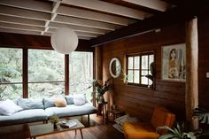 a living room with wood paneling and large windows overlooking the woods in front of it