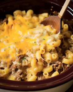 a crock pot full of macaroni and cheese with a wooden spoon in it