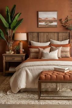 a bedroom with orange walls and white bedding, an ottoman, potted plants, and a painting on the wall