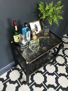 a black and white tiled floor next to a table with liquor bottles on it in front of a gray wall