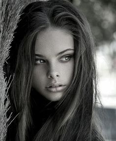 a beautiful young woman leaning against a tree with her hair blowing back and eyes closed