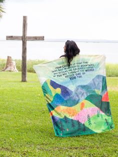 a woman sitting on the grass with a blanket in front of her and a cross behind her