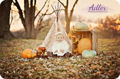 a baby sitting in front of a teepee surrounded by fall leaves