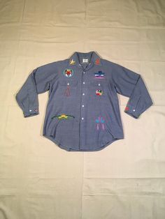 "1970s chambray embroidered men's shirt label- JC Penney Big Mac 65% polyeser, 35% cotton selvedge long sleeve, button up hand embroidered Indiginous North American art/totem/head dress/symbols Polar Bear written/embroidered on back star collars yoke hem good vintage condition, light wear/stains (see photos) measures, lying flat, shoulder-19\" chest-23\" sleeve-23\" length-32\"" Cotton Long Sleeve Shirt With Patches, Cotton Long Sleeve Tops With Patches, Vintage Embroidered Denim Blue Tops, Retro Embroidered Blue Top, Embroidered Denim Blue Cotton Tops, Vintage Blue Cotton Shirt, Blue Cotton Shirt With Embroidered Graphics, Vintage Cotton Shirt For Winter, Retro Blue Embroidered Top