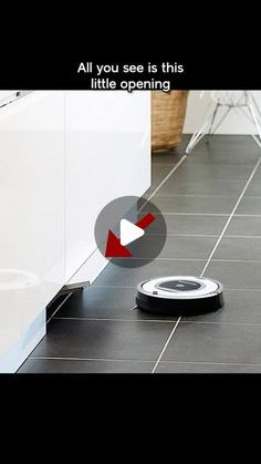 a roomba is on the floor in front of a white cabinet and black tile