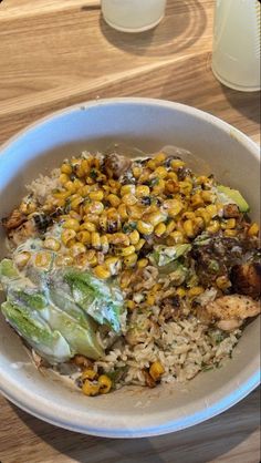 a white bowl filled with rice, corn and lettuce on top of a wooden table