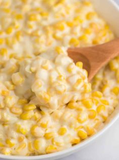 a wooden spoon scooping corn into a bowl with white cheese and sauce on top