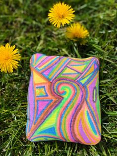 a colorful rock sitting in the grass next to dandelions