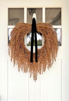 a wreath is hanging on the front door with a black bow around it's neck