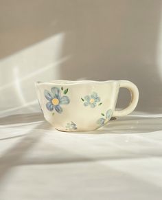 a white cup with blue flowers on it sitting on top of a tableclothed surface