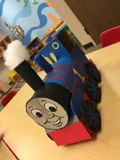 a paper train sitting on top of a wooden table next to a red and blue chair