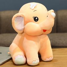 an elephant stuffed animal sitting on top of a wooden table next to a laptop computer