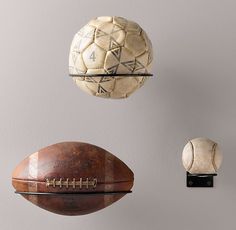 an assortment of sports balls hanging from hooks on a gray wall, including a football