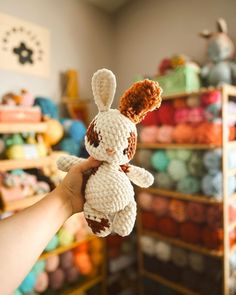 a hand holding a small stuffed animal in front of many crocheted shelves with yarn balls