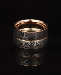 two gold wedding bands with an intricate design on the inside, set against a black background