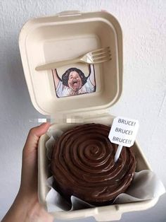 a person holding up a chocolate cupcake in a foam container with a photo on it