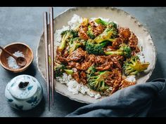 a white plate topped with meat and broccoli on top of rice next to chopsticks